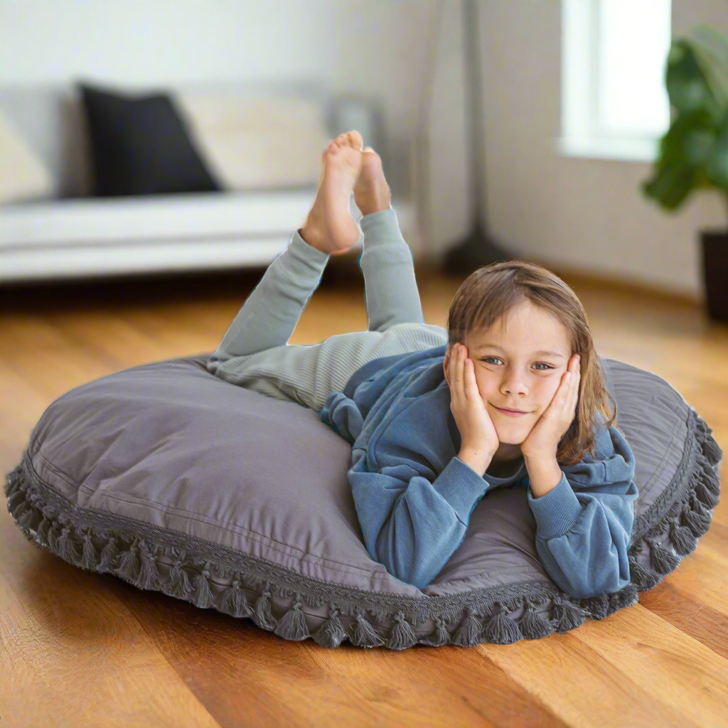 Child lying on their front on large round floor cushion with their feet in the air behind them and their face in their hands