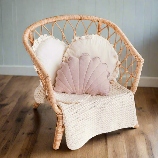 Wicker chair with a shell-shaped pillow and white blanket n a living room setting