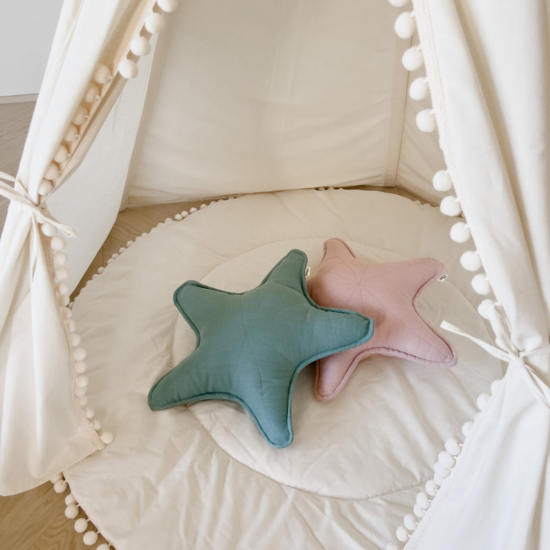 Two star-shaped cushions, one blue and one pink, on a soft surface in a play tent