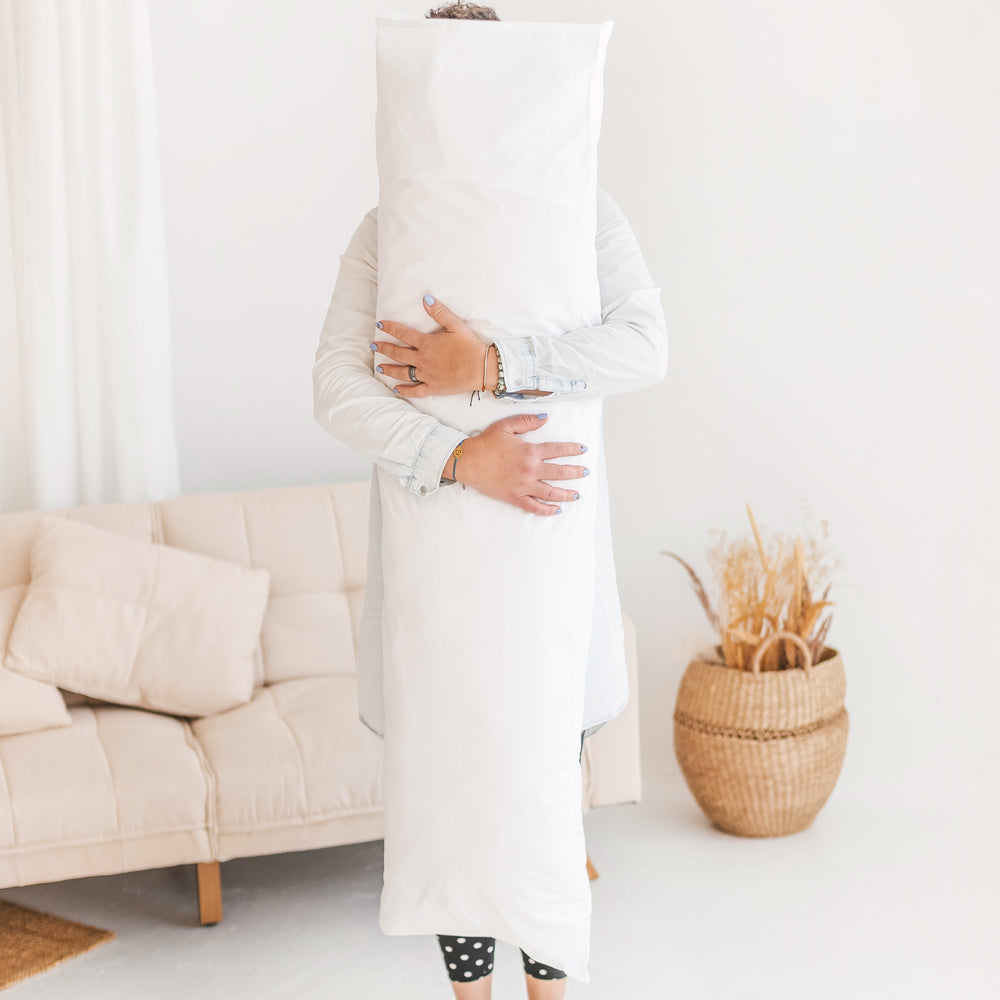 Person holding a large white pillow in a living room setting