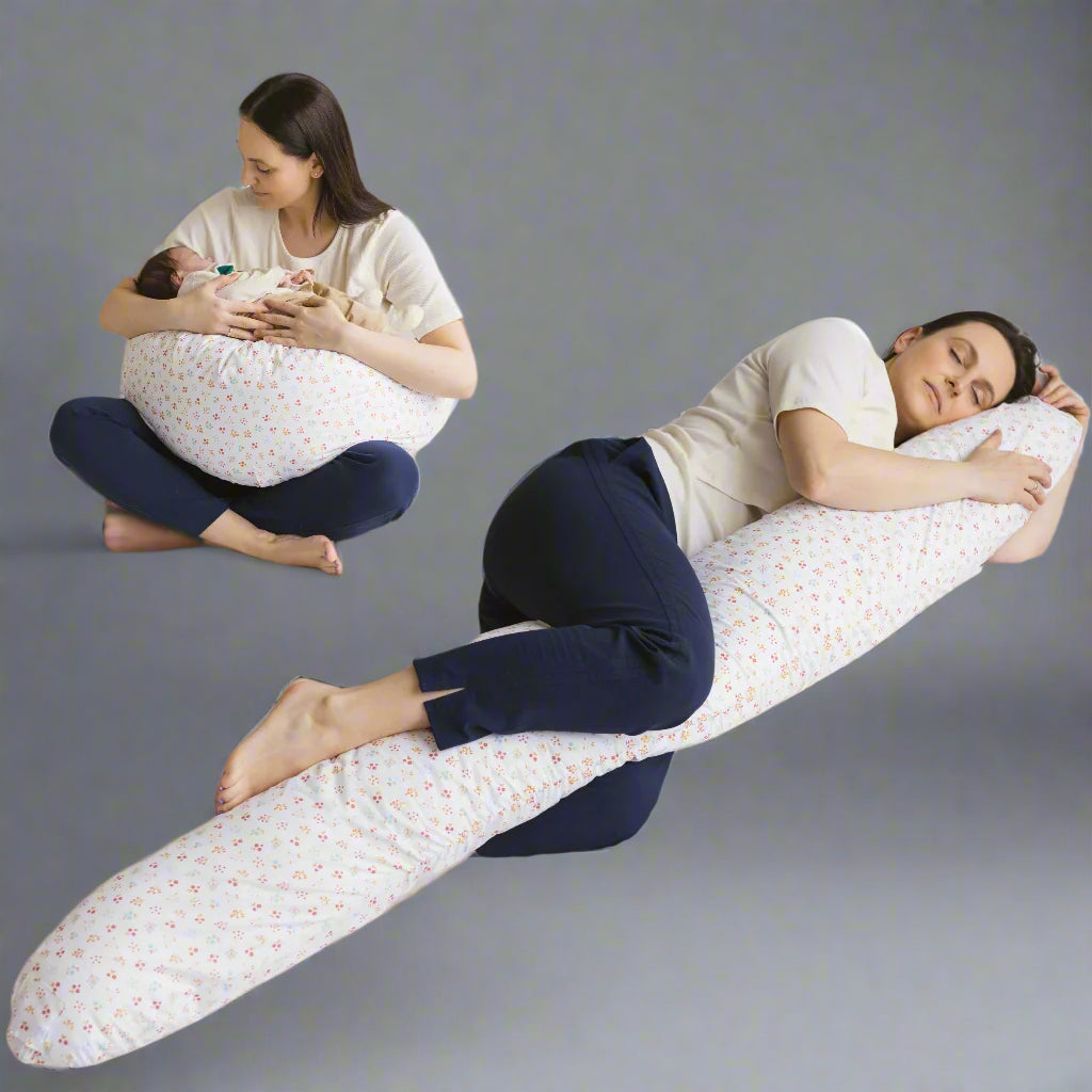 Two images, one of a woman lying down with a support pillow elongated to the full length of her body, and the other image of the same woman sitting cross legged and holding a baby on the support pillow which is on her lap