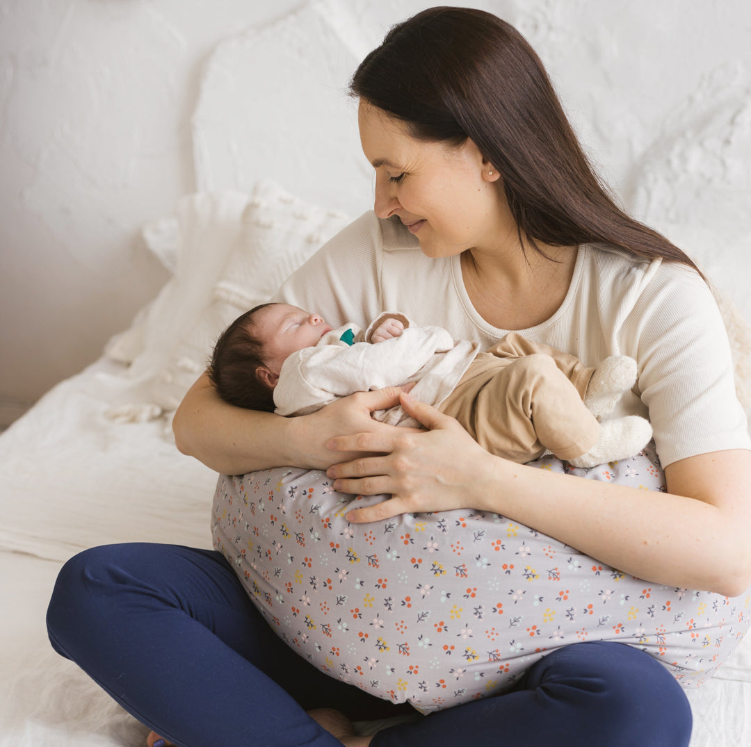 Woman holding a newborn baby on a bed, the woman has her legs crossed with a support pillow on her lap and the baby is resting on it