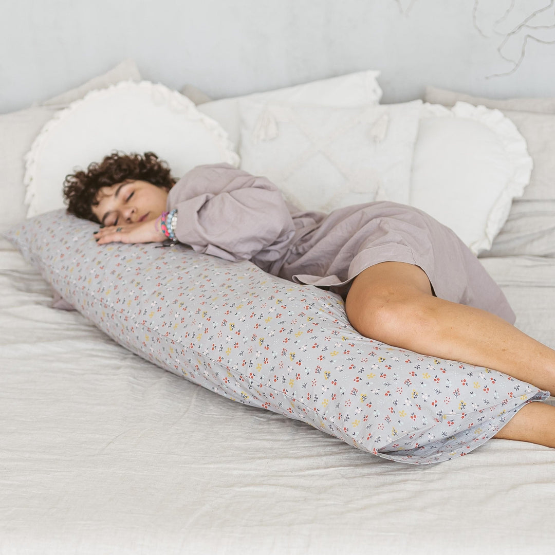 Person lying on a body pillow in bed with a floral pattern