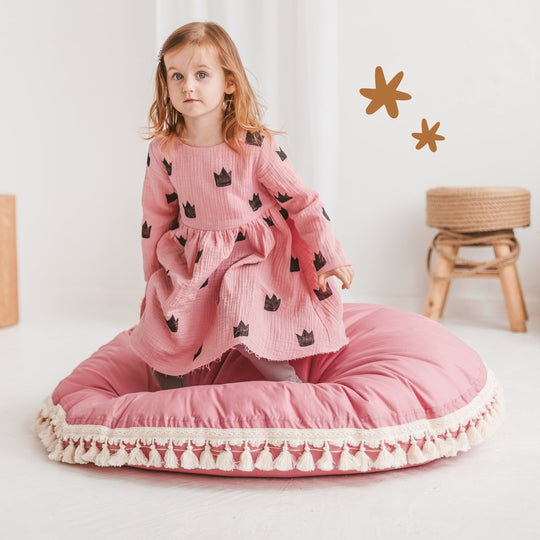 Child sitting on a pink cushion with a white background