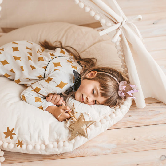 Child lying on large round floor cushion inside a teepee play tent