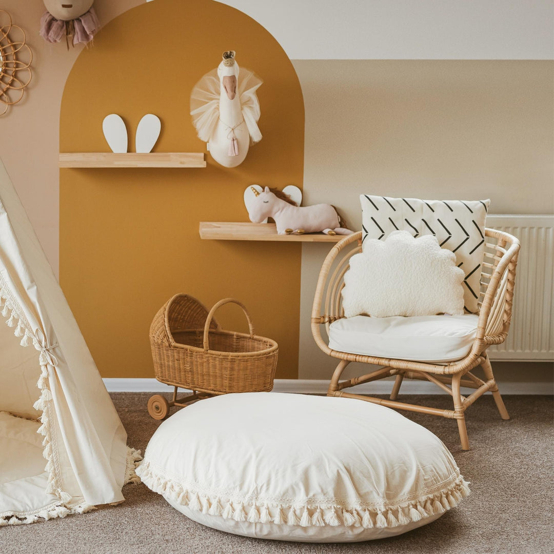 Nursery room with wicker chair, baby crib, and decorative pillows on a neutral colour scheme.