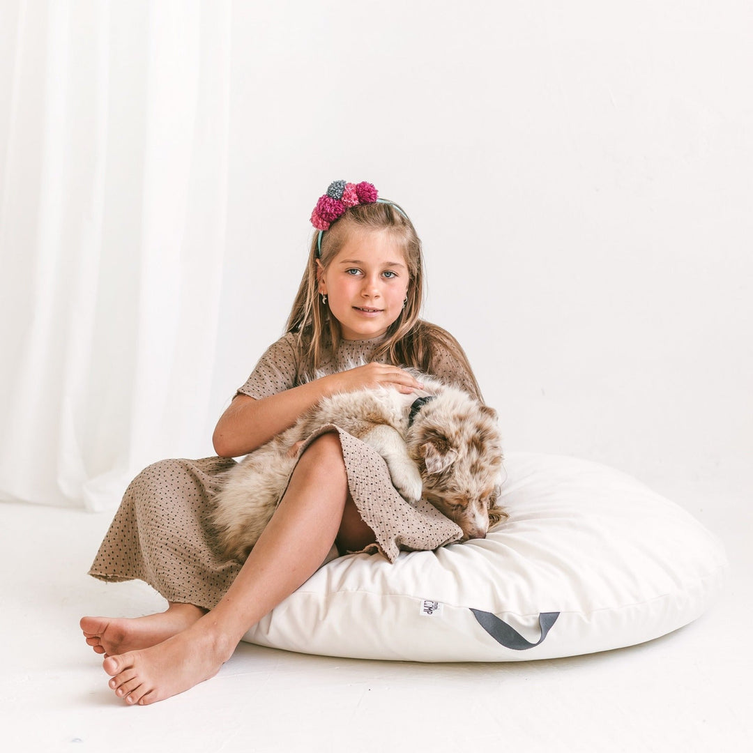 Young girl holding a dog on a white cushion with a white background