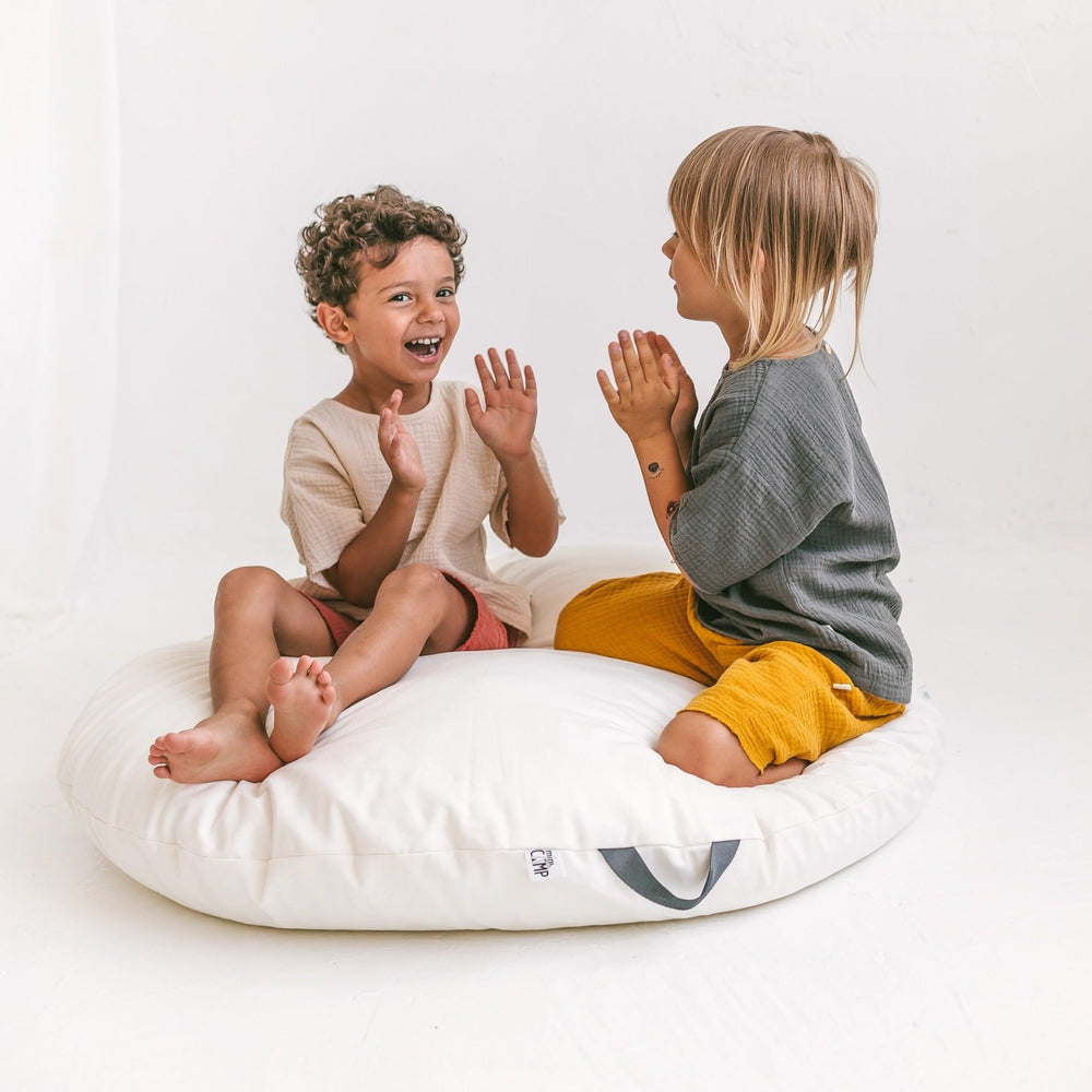 Two children sitting of the white floor cushion and playing a clapping game