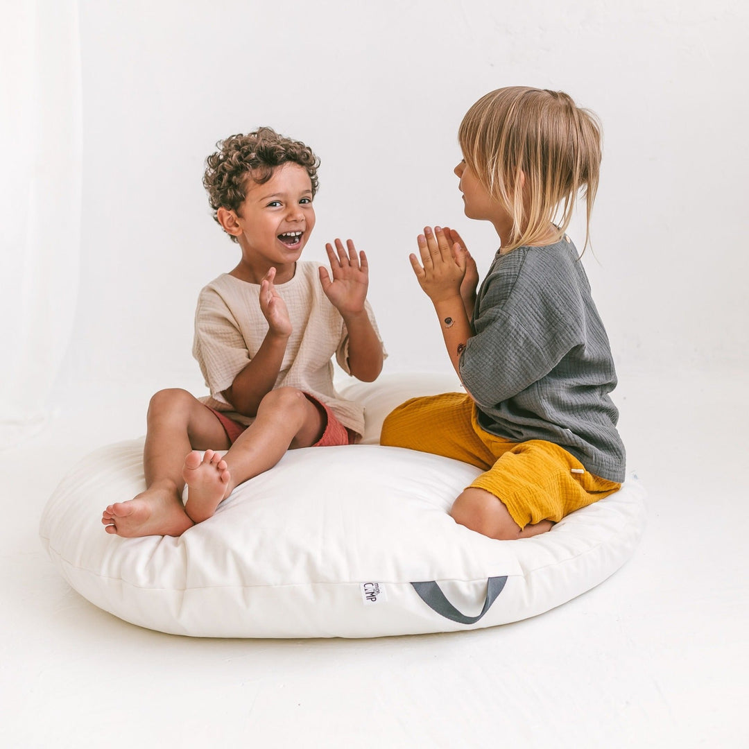 Two children sitting of the white floor cushion and playing a clapping game