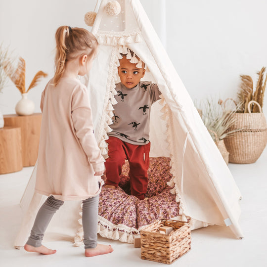 Two children playing inside a white teepee in a bright room with decorative elements.