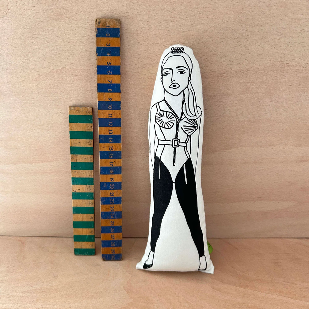 Screen printed doll cushion of Madonna next to two wooden rulers on a wooden background