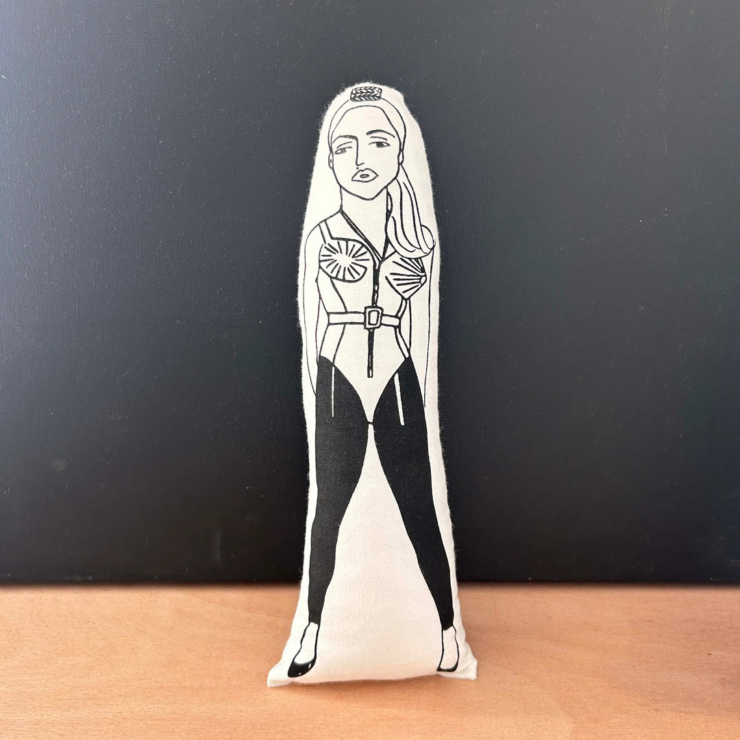 Screen printed doll cushion with white fabric and black illustration depicting musician Madonna, wearing the iconic cone bra