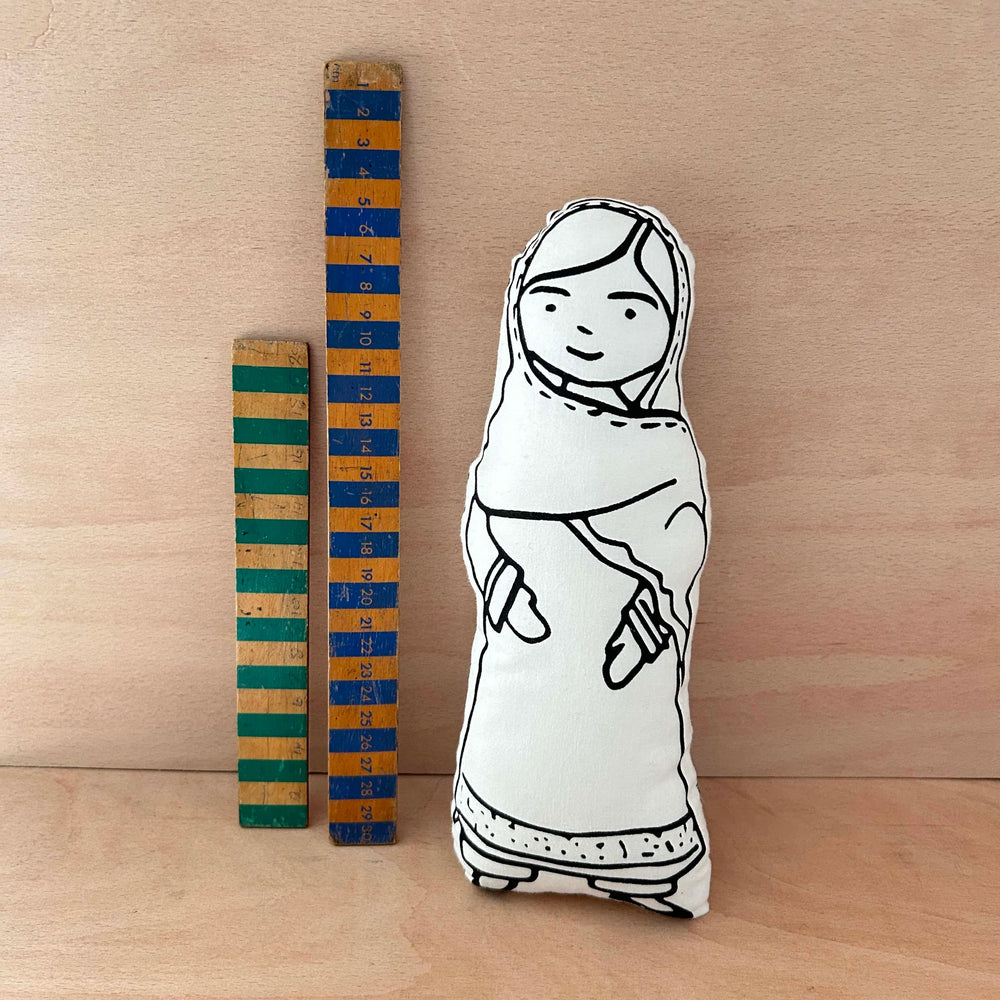 Screen printed doll cushion of activist Malala Yousafzai next to two wooden rulers on a wooden background