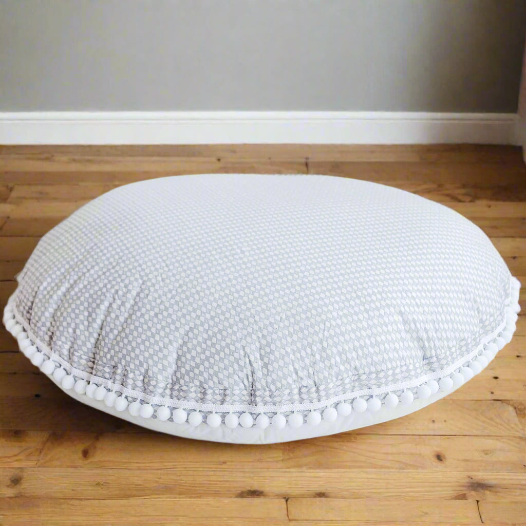 Round floor cushion in light grey colour and delicate diamond design with pom-pom trim