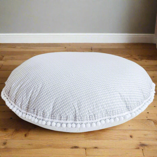 Round floor cushion in light grey colour and delicate diamond design with pom-pom trim