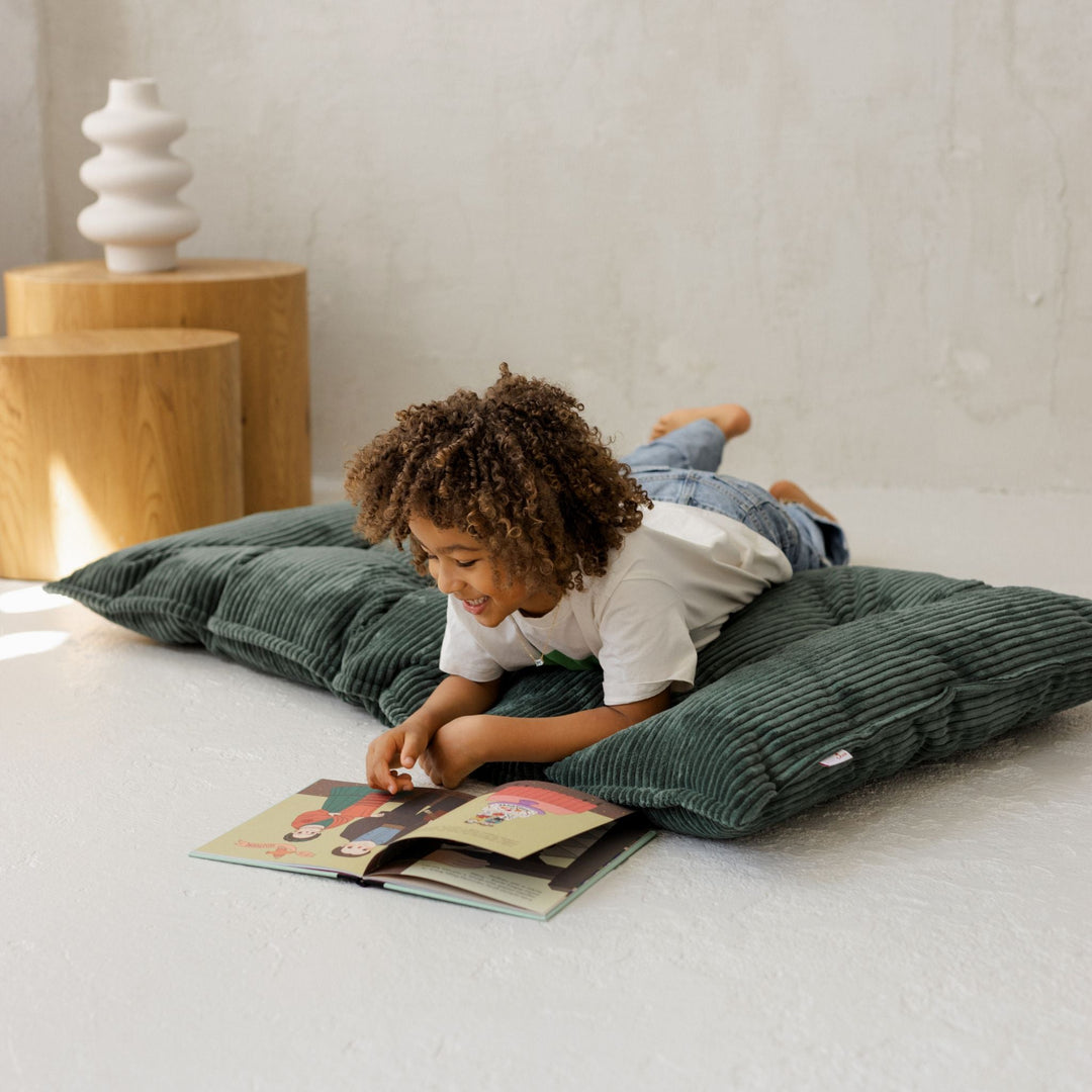 Child reading a book on a green cushion in a cosy room.