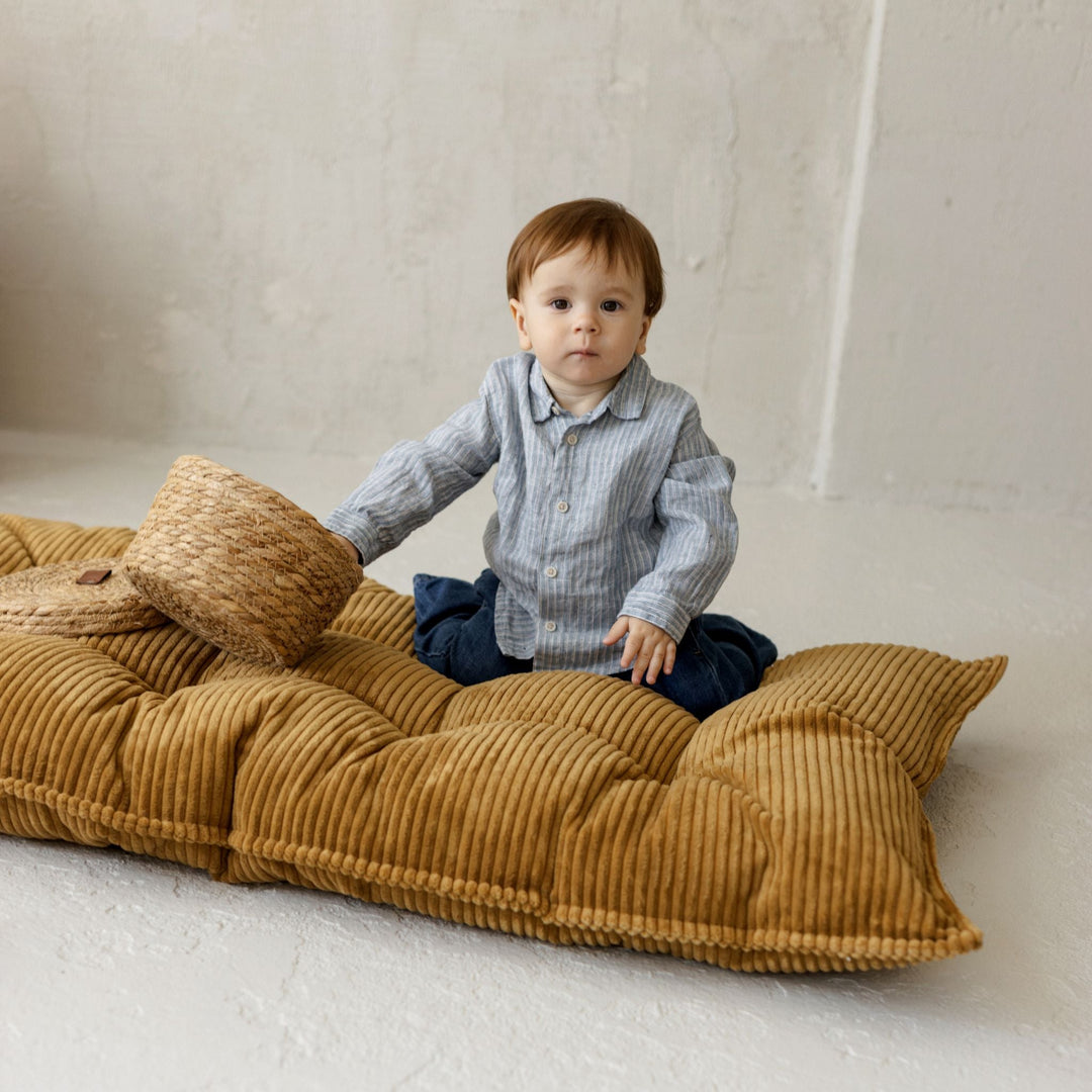 Child sitting on a long mustard-coloured cushion with a textured corduroy surface.