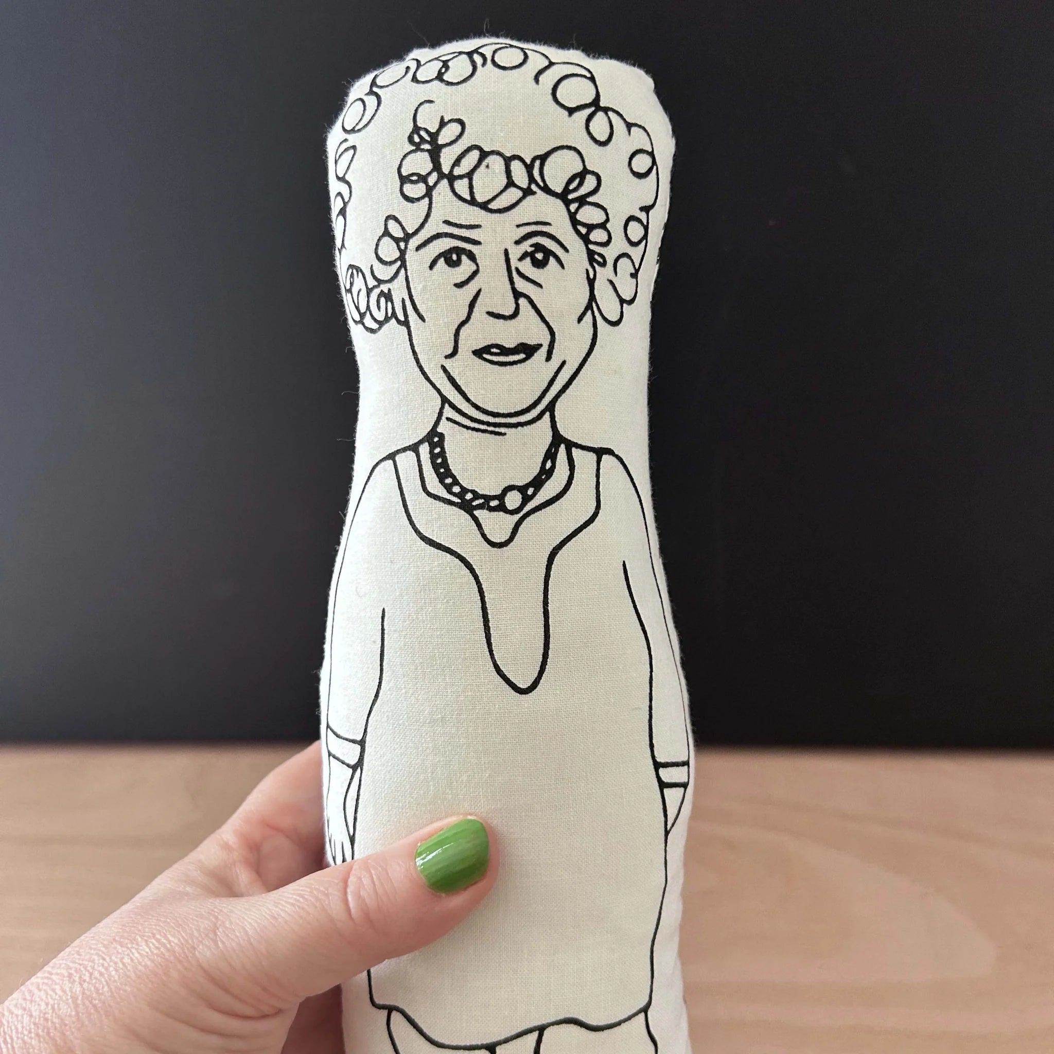 Hand holding a screen printed doll cushion with white fabric and black illustration depicting actor Miriam Margolyes, wearing a dress and chunky necklace