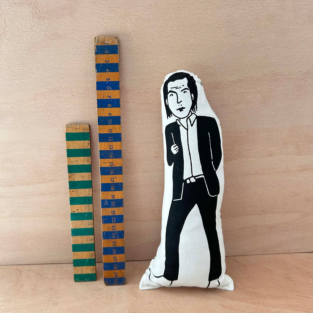 Screen printed doll cushion of musician Nick Cave next to two wooden rulers against a wooden background