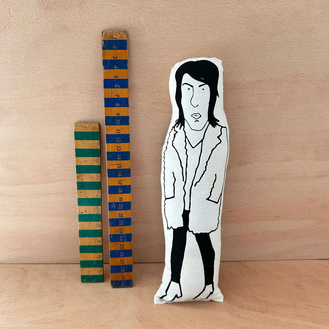 Screen printed doll cushion of Noel Fielding next to two wooden rulers on a wooden background
