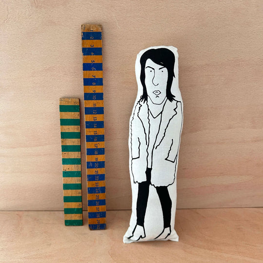 Screen printed doll cushion of Noel Fielding next to two wooden rulers on a wooden background