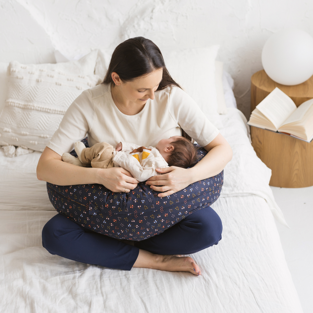 Woman holding a baby in a nursing pillow on a bed