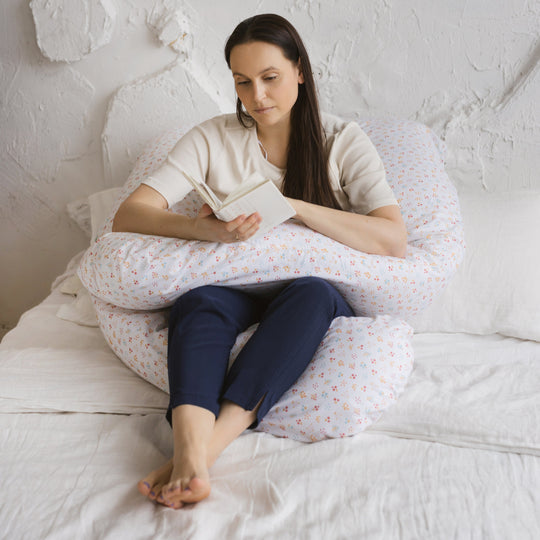 A woman reading with the support pillow wrapped around her back and onto her lap supporting her book and legs from underneath