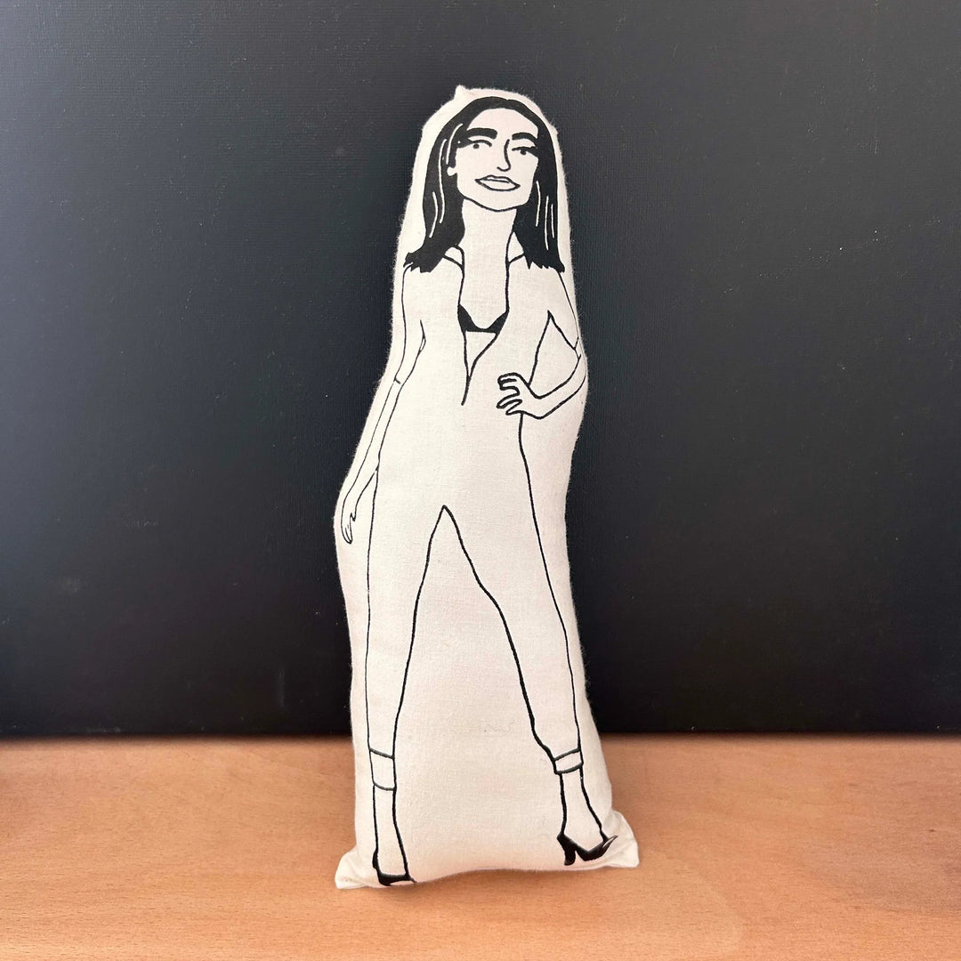 Screen printed doll cushion with white fabric and a black illustrated figure depicting musician PJ Harvey wearing her iconic cat suit