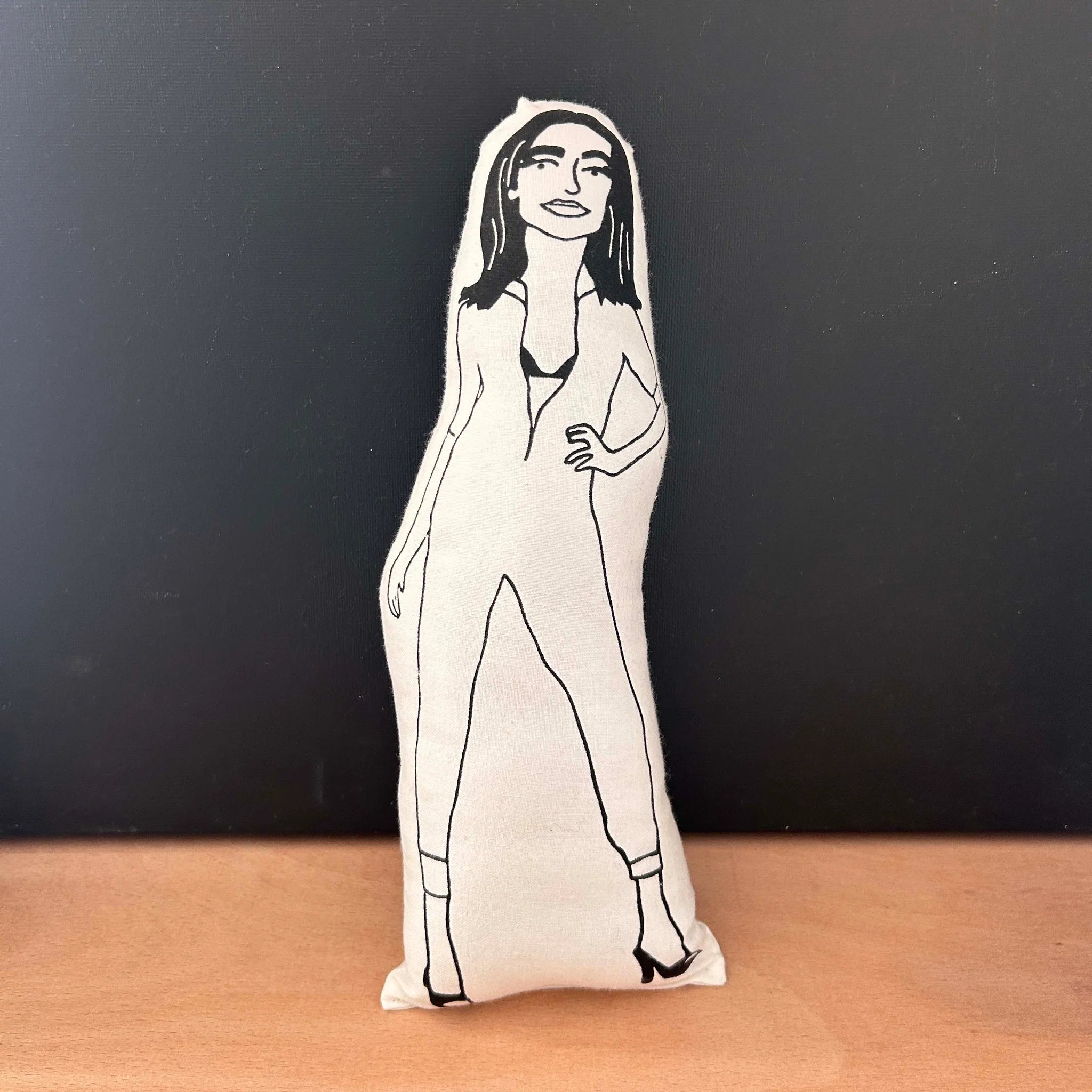 Screen printed doll cushion with white fabric and a black illustrated figure depicting musician PJ Harvey wearing her iconic cat suit