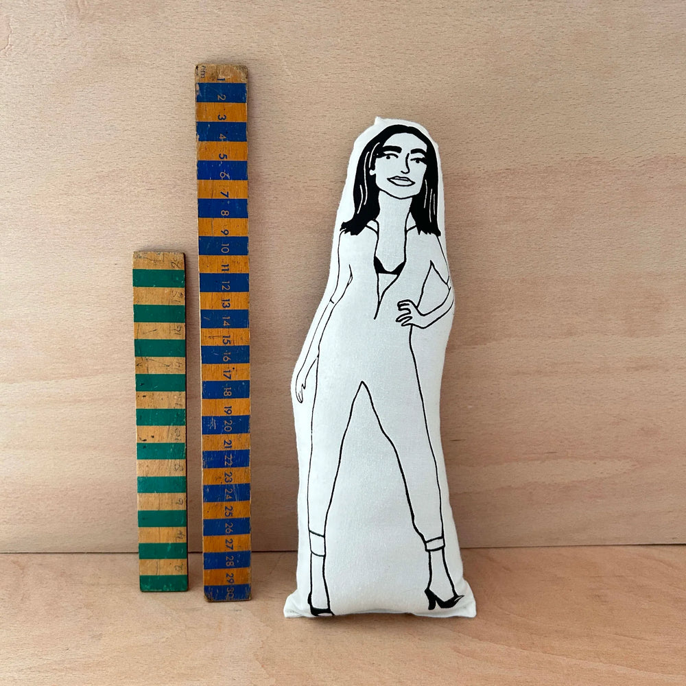 Screen printed doll cushion with black and white illustration of musician PJ Harvey next to two wooden rulers on a wooden surface.