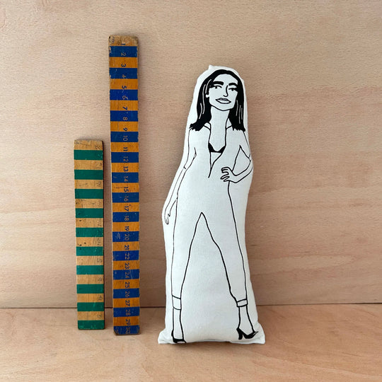 Screen printed doll cushion with black and white illustration of musician PJ Harvey next to two wooden rulers on a wooden surface.