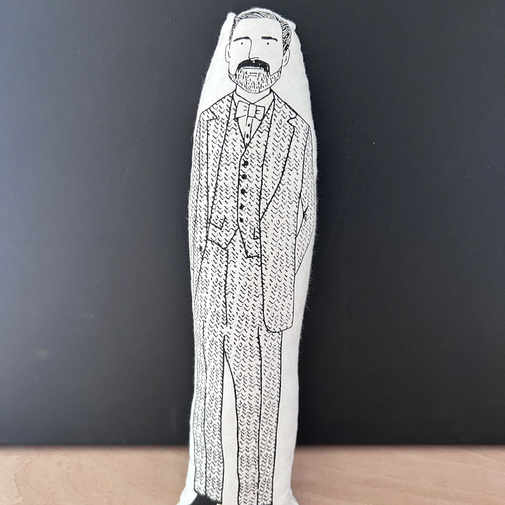 Screen printed doll cushion with white fabric and black illustration depicting Patrick Grant from the Great British Sewing Bee wearing a three-piece tweed suit and bow tie