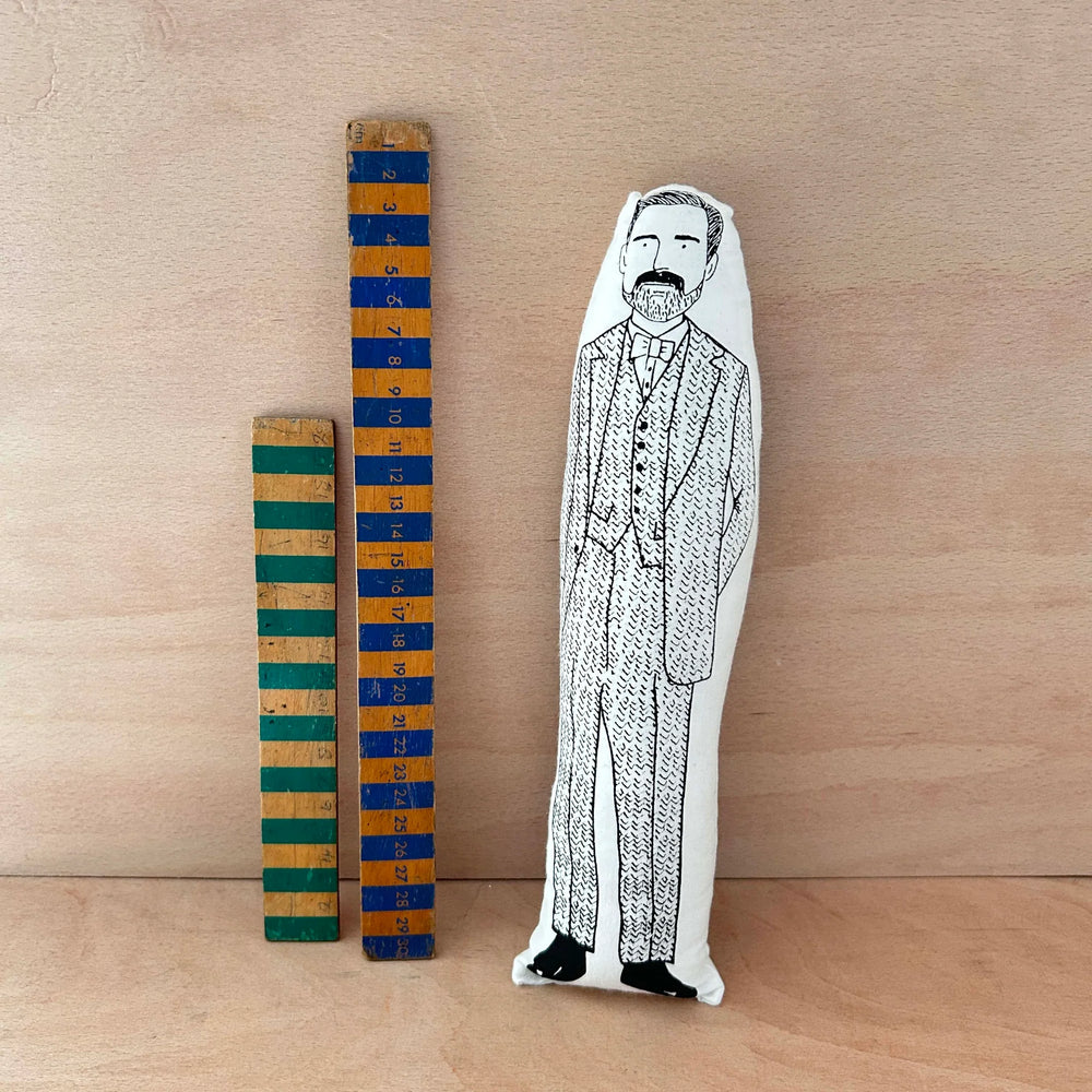 Screen printed doll cushion of TV presenter  and fashion designer Patrick Grant next to two wooden rulers on a wooden background