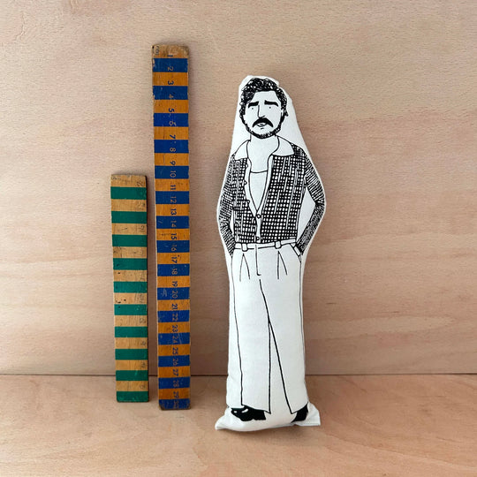 Screen printed doll cushion of Pedro Pascal next to two wooden rulerson a wooden background