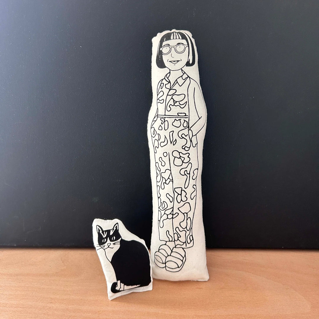 Two screen printed doll cushions, both with white fabric and black drawn illustration, one depicting physchotherapist and columnist Philippa Perry wearing a patterned jumpsuit and the other smaller one is her black and white cat, Kevin