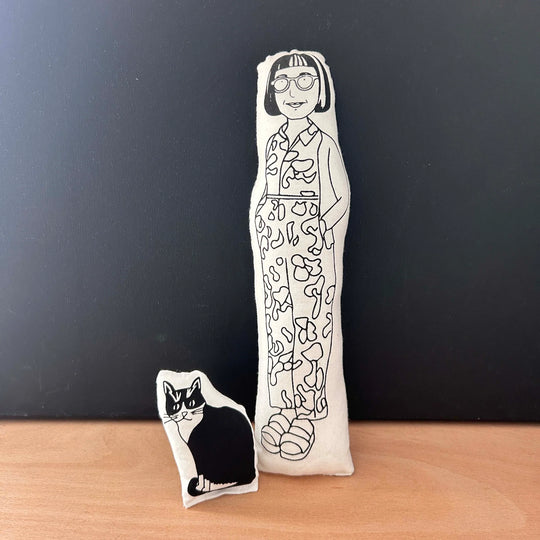 Two screen printed doll cushions, both with white fabric and black drawn illustration, one depicting physchotherapist and columnist Philippa Perry wearing a patterned jumpsuit and the other smaller one is her black and white cat, Kevin
