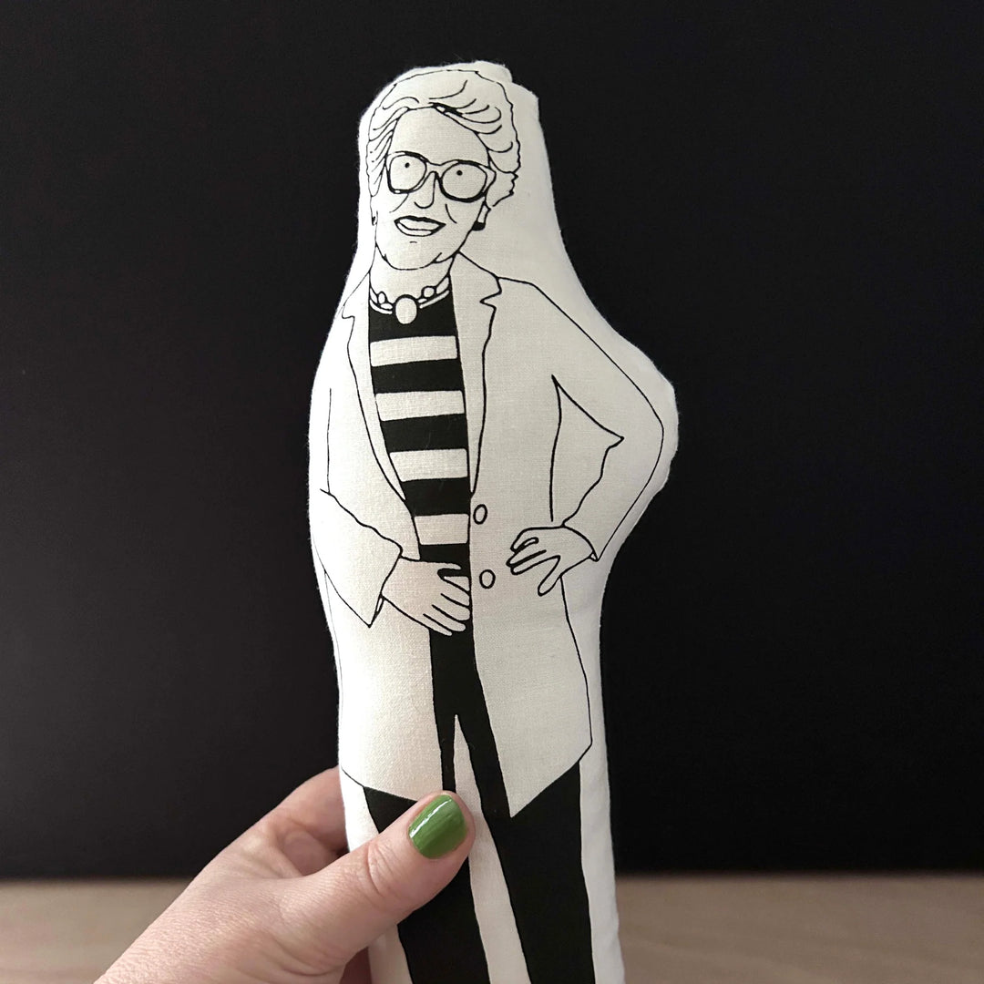 Hand holding screen printed doll of Prue Leith against a dark background