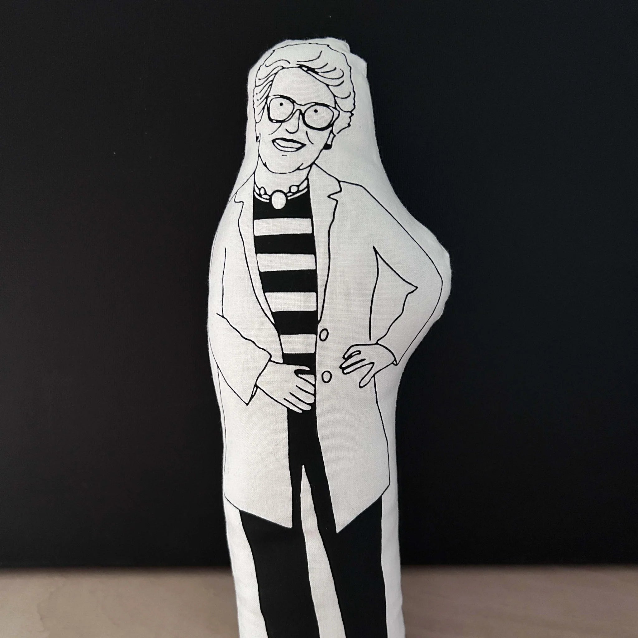 Screen printed doll cushion with white fabric and black drawn illustration depicting TV presenter Prue Leith wearing an oversized jacket, a striped top, large glasses and chunky necklace