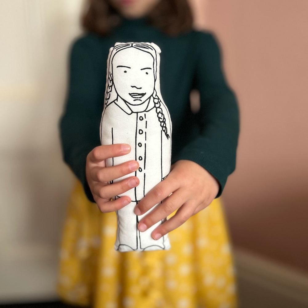 A child holding out screen printed doll cushion of climate activist Greta Thunberg towards the camera