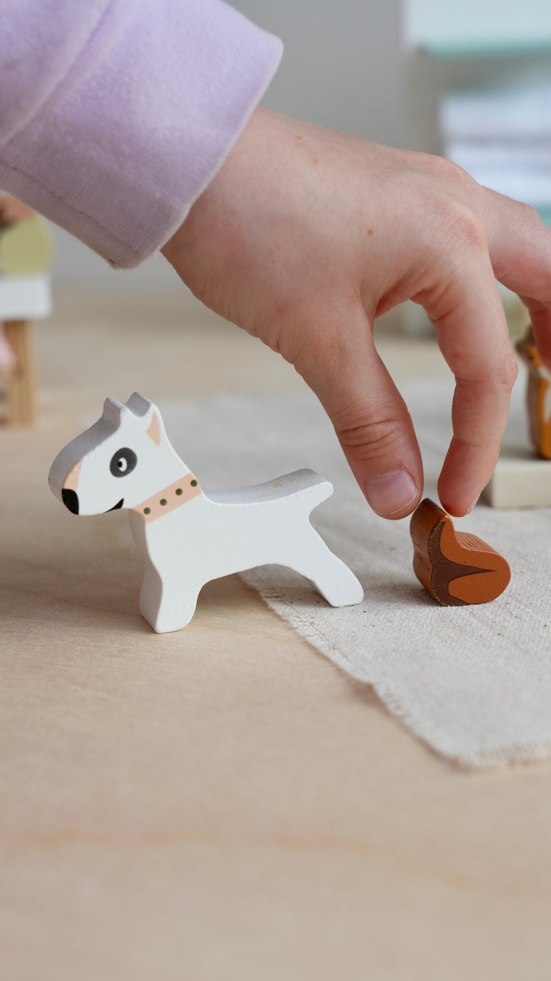 Hand interacting with a small wooden dog figurine on a light surface