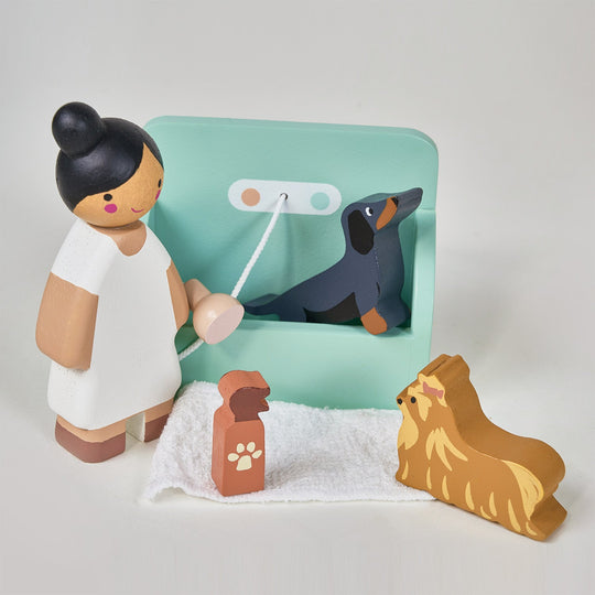 Wooden toy figure of a person with a dog and a leash on a light gray background
