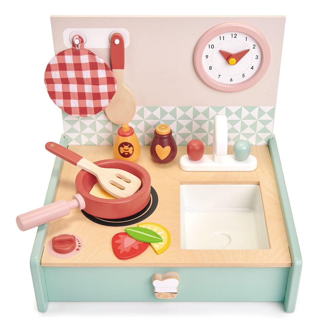 Wooden toy kitchen set with various utensils and a clock on a white background