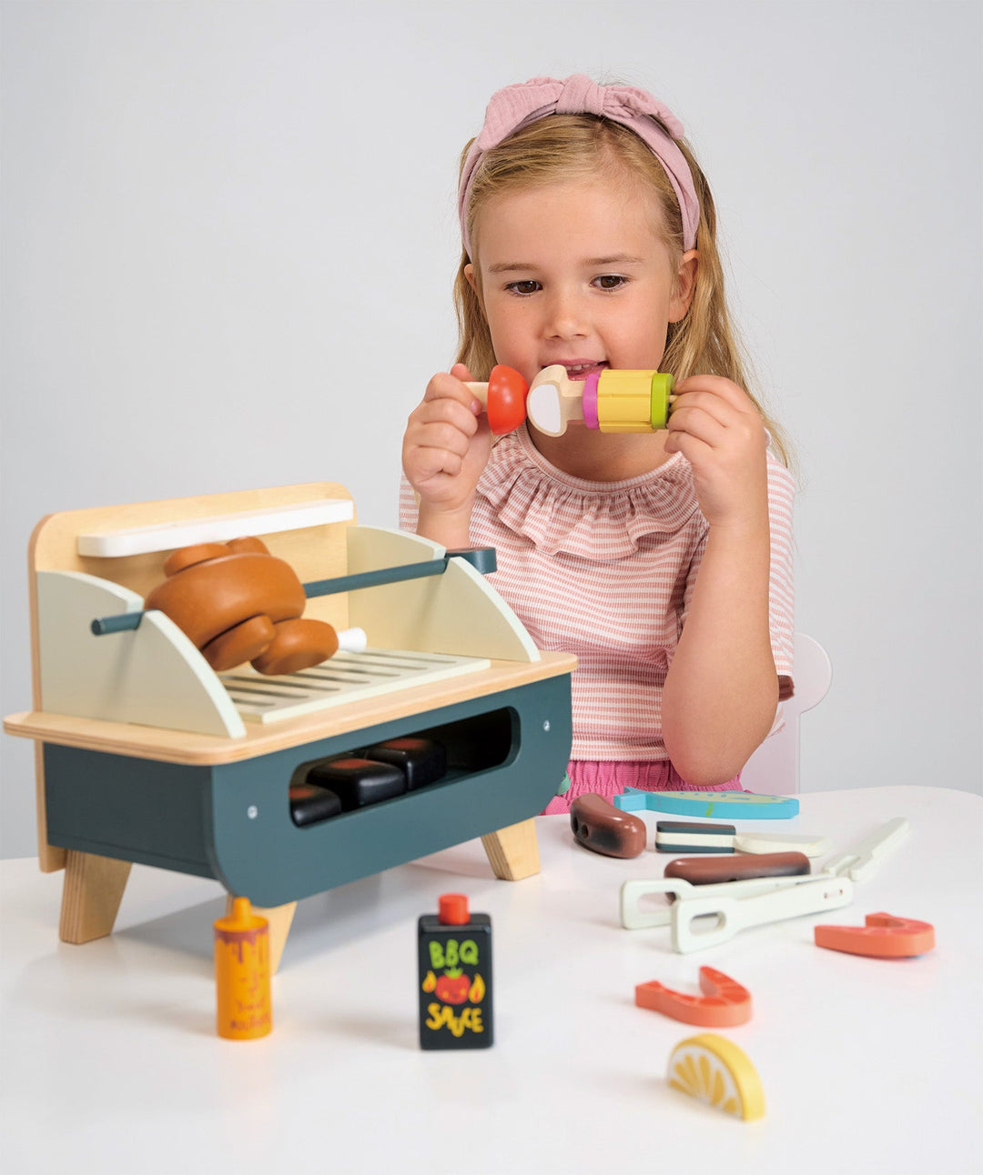 Child playing with a toy grill set on a white surface