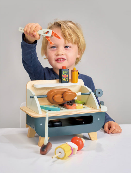 Child playing with a toy grill set on a plain background
