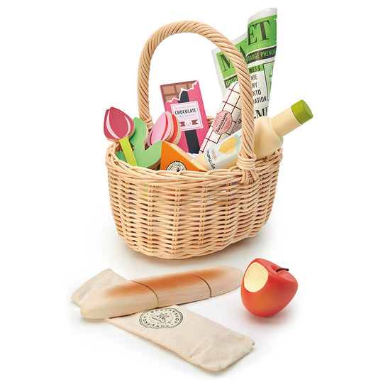 Wicker picnic basket with toys, newspaper, and apple on a white background