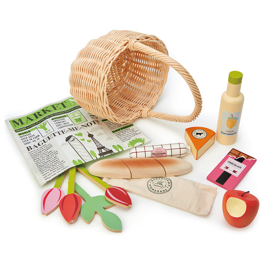Wooden toy set with a wicker basket, newspaper, bread, cheese, and other food items on a white background