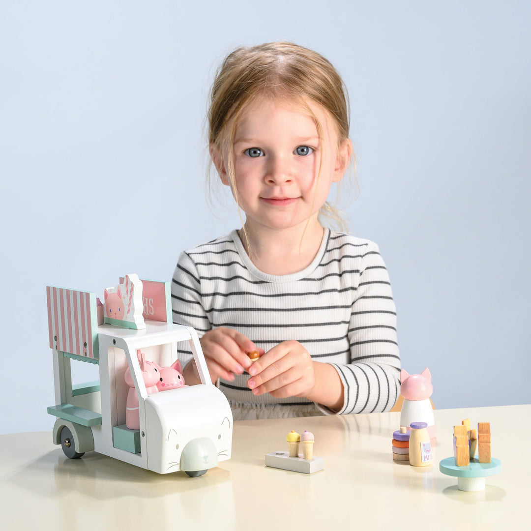Child playing with a toy milkshake cart and figurines on a light blue background