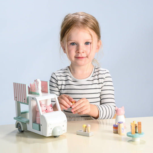 Child playing with a toy milkshake cart and figurines on a light blue background