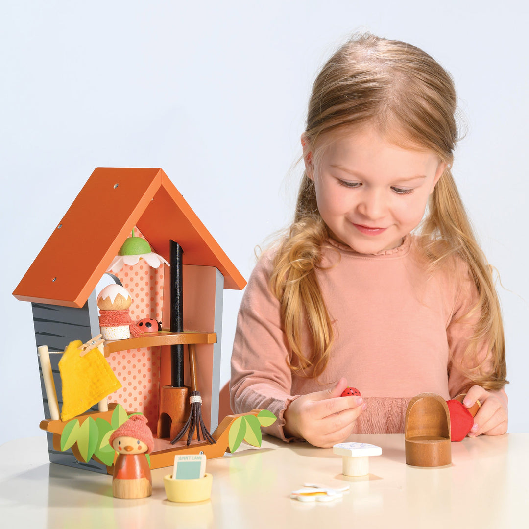 Young girl playing with a wooden 
 bird house and accessories on a light blue background