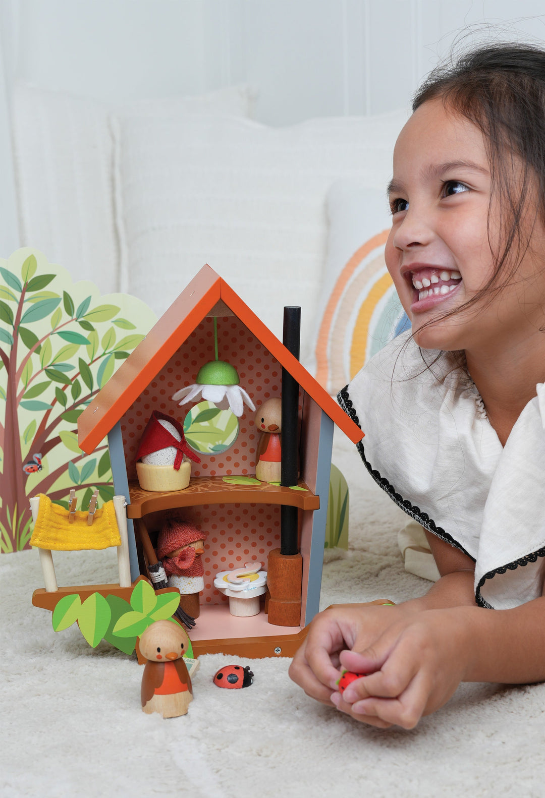 Child playing with a toy bird house and figurines on a white surface.